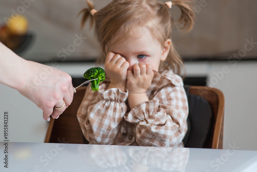 Tableau sur toile Mom is spoon-feeding a little girl broccoli