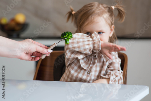 Mom is spoon-feeding a little girl broccoli. The child refuses to eat. Baby food. Healthy food.