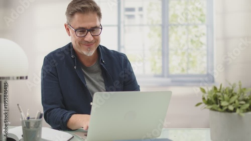 Casual businessman working with laptop computer in home office, happy, smiling. Portrait of middle age man in 50s, white caucasian, gray hair.