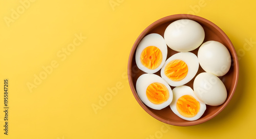 Hard boiled eggs whole and halved in a bowl on yellow background