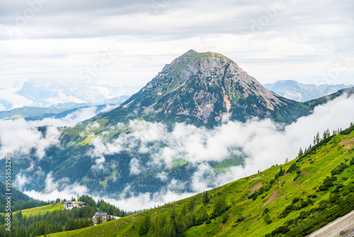 Majestic mountains rise above the rolling clouds in the Low Tauern region of Austria. Lush green hills contrast with rocky peaks, offering a stunning view of nature's beauty.
