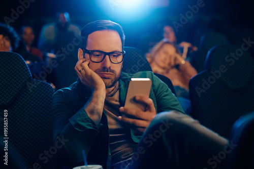 Tableau sur toile Bored man using cell phone in movie theater.