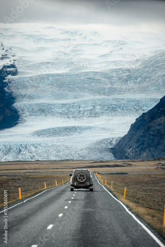 Obraz na płótnie Camioneta viajando en una carretera de Islandia con vista a un glaciar y montañas nevadas al fondo