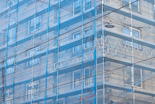 Картината върху платно Building facade covered in blue scaffolding netting with visible windows and str