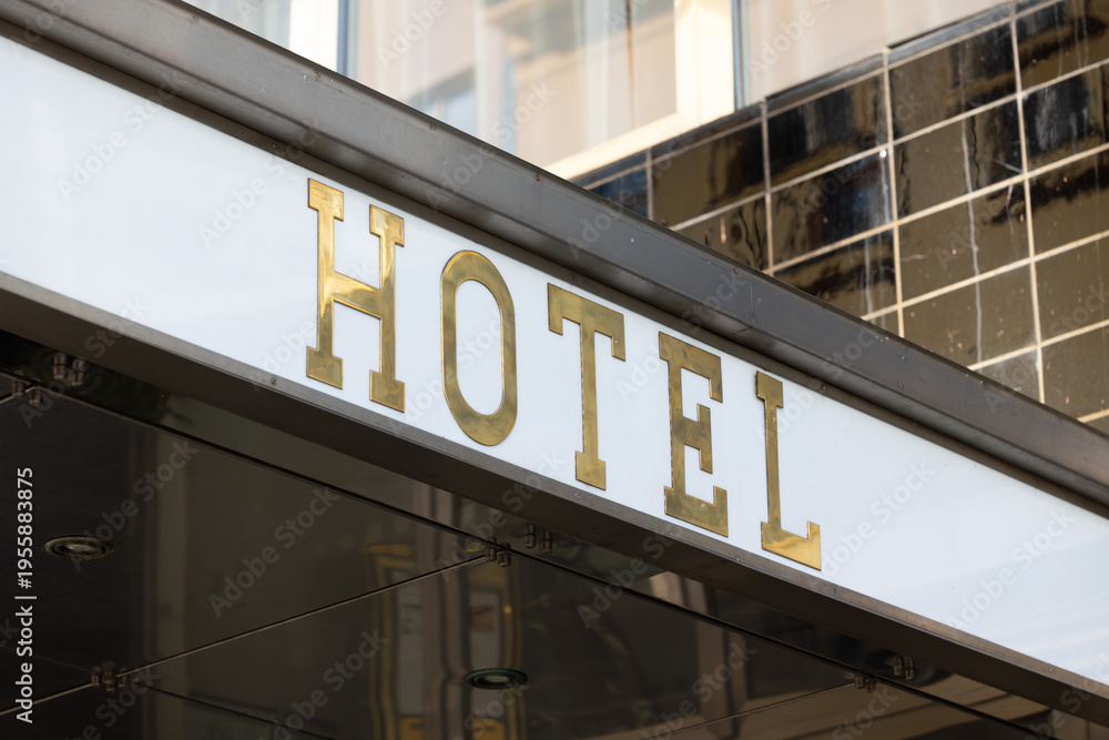 Fototapeta premium Hotel entrance sign with gold lettering against a modern glass facade, showcasing a contemporary architectural design in an urban setting