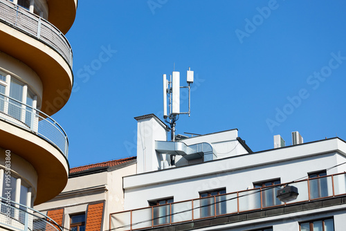 4G 5G 6G Telecommunications antenna mounted on a rooftop of a modern building with curved balcony and clear blue sky in the background