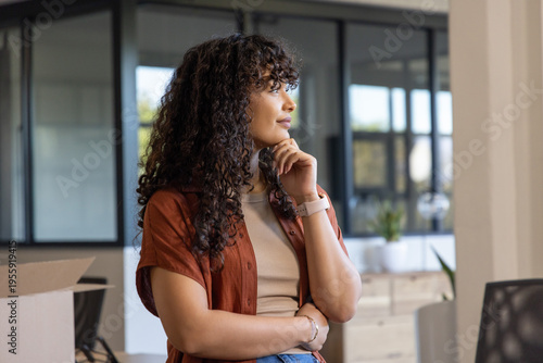 Картината върху платно Female office worker standing in modern office wearing rust top near box, lookin