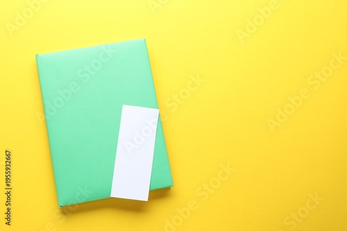 Book with white bookmark on yellow background, top view. Space for text