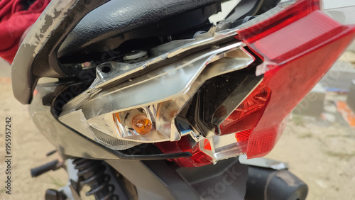 Close-up of a shattered motorcycle rear turn signal and brake light housing. Visible orange bulb and cracked red plastic casing from a vehicle accident impact.