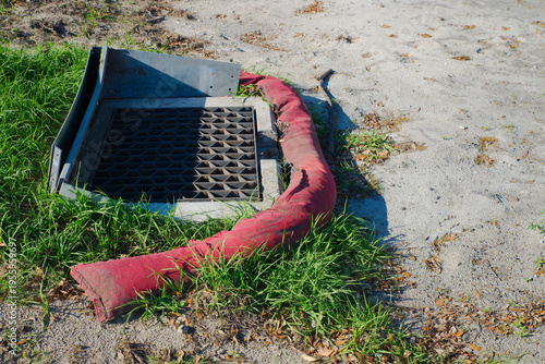 Cuadro en lienzo A metal storm drain grate surrounded by a red silt sock on sandy soil and grass, illustrating erosion control, stormwater protection and roadside drainage maintenance at a construction or urban site