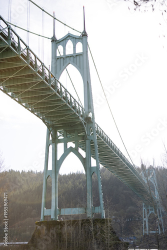 Vintage bridge arches over calm water. Steel structure gleams under soft morning light. Lush trees line distant shore. Quiet, sturdy, timeless engineering stands tall. Ideal for travel, heritage, arch