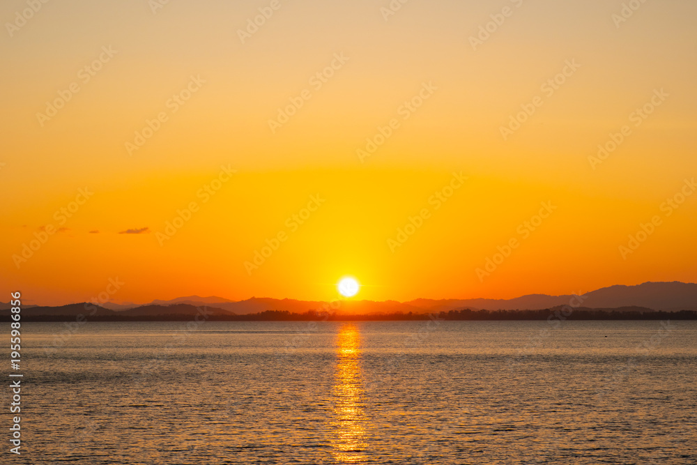 Obraz premium nature sky breathtaking golden sunset over a calm ocean, with the entire sky and water bathed in brilliant shades of yellow and orange. Streaky clouds enhance the dramatic display 