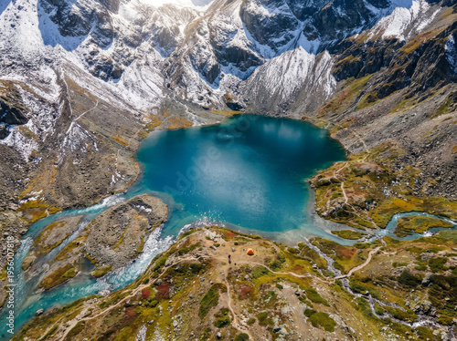 Stunning aerial view of a vibrant blue alpine lake surrounded by rugged, snow-capped mountains and winding rivers.