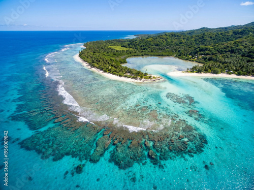 Aerial view of a tropical island coastline with lush green jungle and clear turquoise waters showcasing coral reefs.