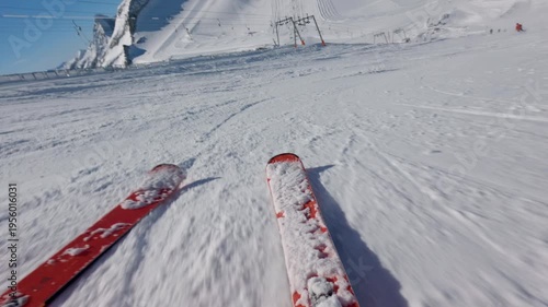 Low angle POV of skier going fast down the hill on sunny clear day. Skis visible in the foreground