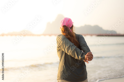 Rear view of unrecognizable woman stretching arms on beach during sunrise wellness routine
