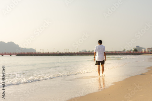 Rear view of man walking on tropical beach shoreline towards a new journey