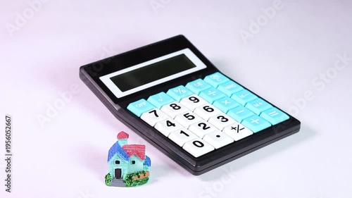 白背景で回転するミニチュアハウスと電卓の映像