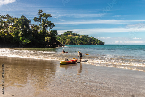 Coastal landscape with a couple of tourists kayaking on the beach on a sunny day with turquoise sea and tropical vegetation in Quepos, Puntarenas province, Costa Rica