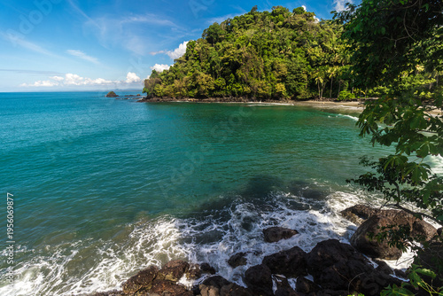 Rocky coastal landscape with waves on the beach and turquoise sea with tropical vegetation of Quepos in the province of Puntarenas, Costa Rica
