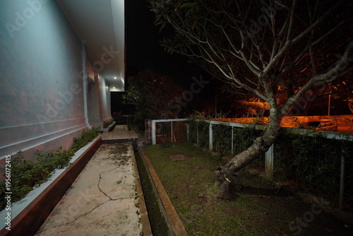Tableau sur toile Nighttime view of a pathway beside a building with a tree and a fence in a dimly