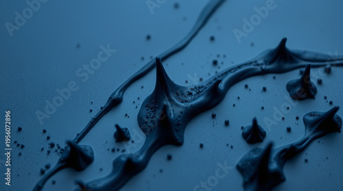 Deep blue background with flowing black viscous liquid creating sharp protrusions and tiny particles, illuminated by dra