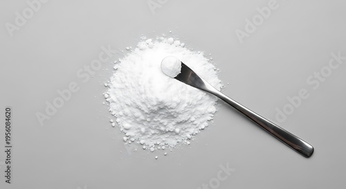 A small metal spatula resting on a neat pile of white powdered substance on a grey background. allantoin