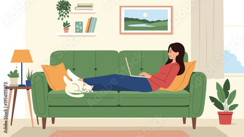 Relaxed woman lying on a comfortable green sofa and working on her laptop while her white cat sleeps peacefully on her legs.