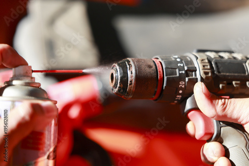 Focused worker performing maintenance on power drill. mechanic hand spraying lubricant for tool repair in garage, cleaning equipment with professional care