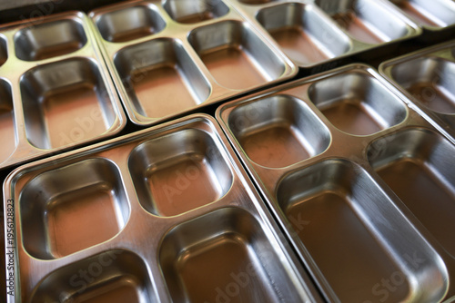 Close up view of empty metal compartment food tray in row at school or prison cafeteria. feeling of institutional routine and emptiness conveyed by shiny, sterile trays