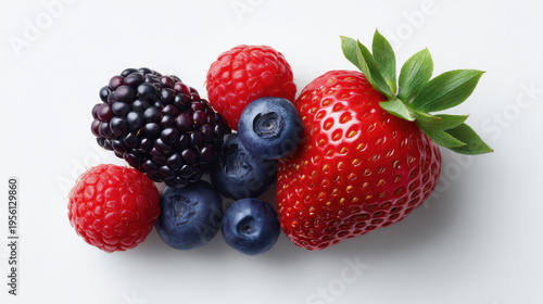 A fresh and colorful assortment of ripe berries including a strawberry, raspberries, blueberries, and a blackberry arranged on a simple white surface together.