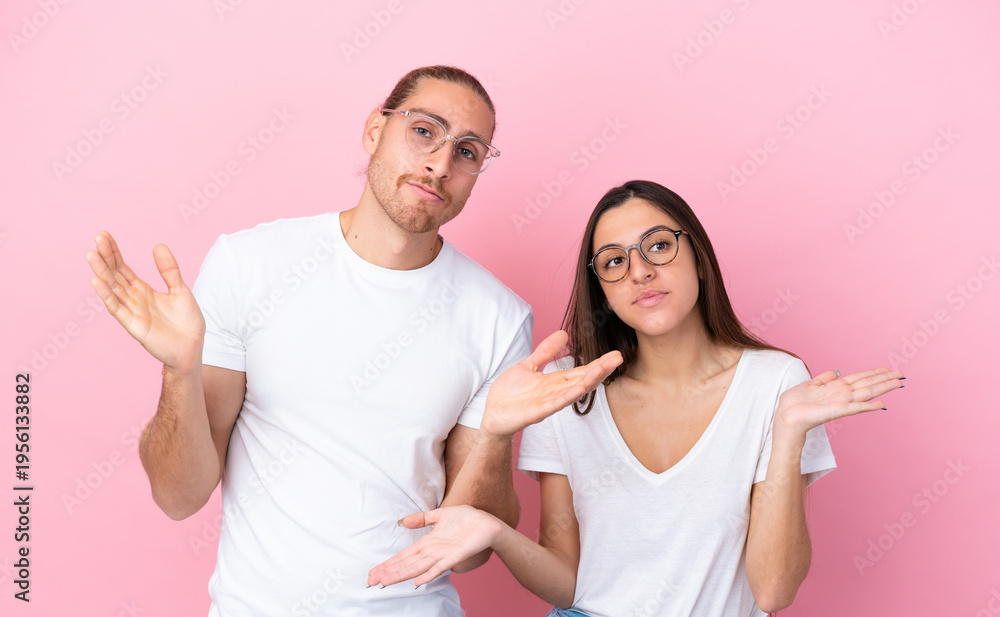 Fototapeta premium Young caucasian couple isolated on pink background With glasses and having doubts