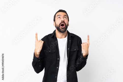 Young man with beard over isolated white background surprised and pointing up