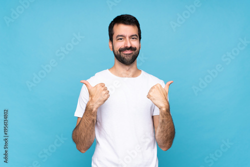 Young man with beard  over isolated blue background with thumbs up gesture and smiling
