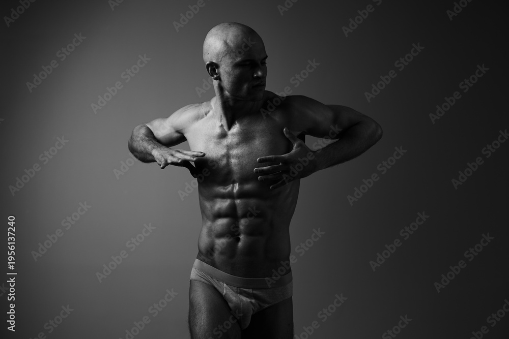 Fototapeta premium Black and white image of a muscular man posing confidently, showcasing his physique and strength with dramatic lighting.