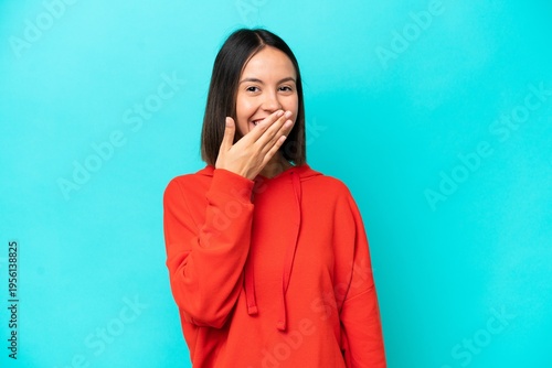 Young caucasian woman isolated on blue background happy and smiling covering mouth with hand