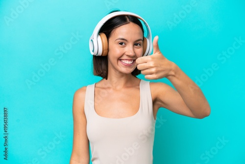 Young caucasian woman isolated on blue background listening music and with thumb up