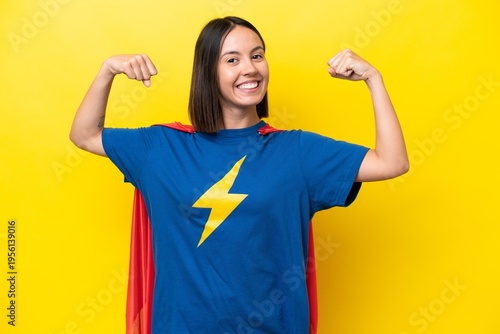 Young caucasian woman isolated on yellow background in superhero costume and doing strong gesture