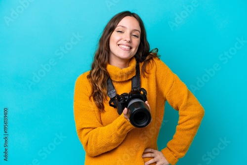 Young photographer woman isolated on blue background posing with arms at hip and smiling