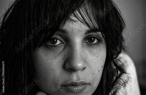 Black and white portrait of a woman with dark hair and intense eyes. She gazes directly at the camera with a serious expression. Hair falls loosely around her face in soft waves