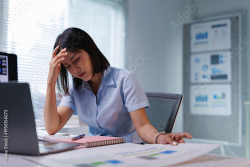 Canvastavla Young Asian woman at office desk late at night holding her head, exhausted and o