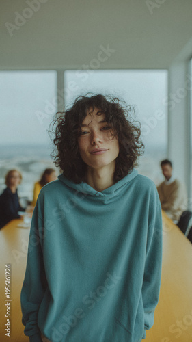 Young woman with curly hair smiling in casual sweatshirt in modern office meeting room background for portrait and business profile design