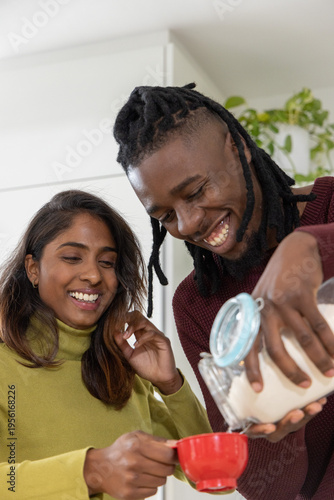 Couple African American and Indian pouring powder from glass jar into red cup at kitchen counter