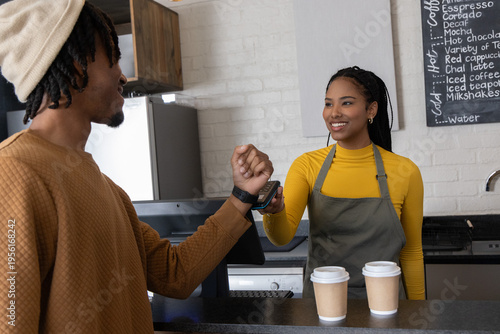African American customer and barista tapping smartwatch at counter with card reader, olive apron