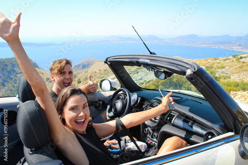 Fotografie Happy couple enjoying road trip in convertible car with sea view
