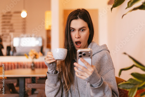 Tableau sur toile Unbelievably shocked young woman in grey hoodie holding white cup of coffee and