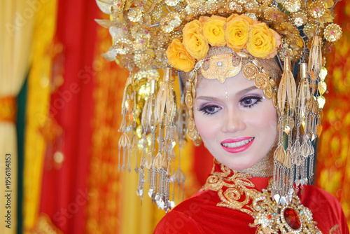 Close-up of a beautiful Acehnese bride wearing a majestic golden headdress and intricate red traditional wedding attire, smiling radiantly