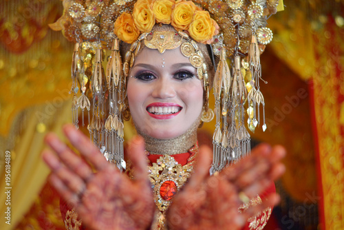 Close-up of a beautiful Acehnese bride wearing a majestic golden headdress and intricate red traditional wedding attire, smiling radiantly