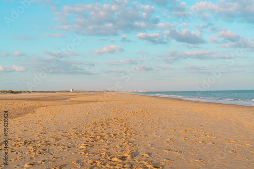 Wide sandy beach under a bright blue sky with scattered clouds.