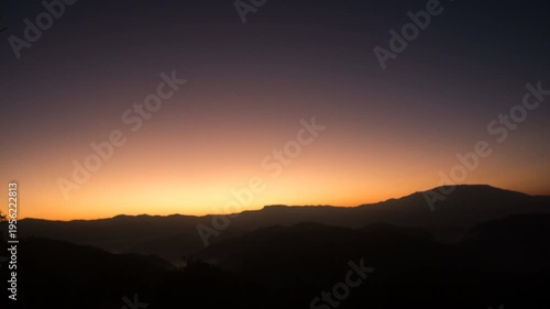 A mesmerizing sunset over the silhouettes of majestic mountains paints the sky with vibrant colors, evoking a sense of tranquility.